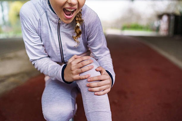 Teenage girl suffering knee injury while jogging outdoors