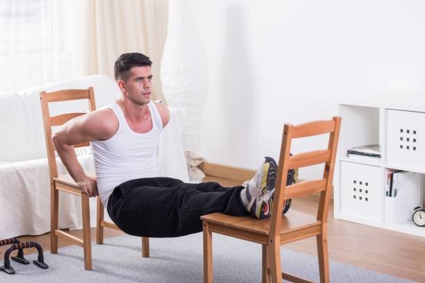 Handsome man during physical exercises at home, using chairs for his training