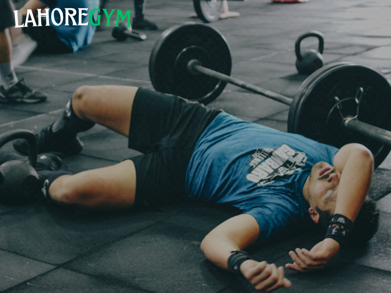 Exhausted athlete showing overtraining symptoms in the gym Tired male athlete sitting on gym floor after intense workout, showing signs of overtraining