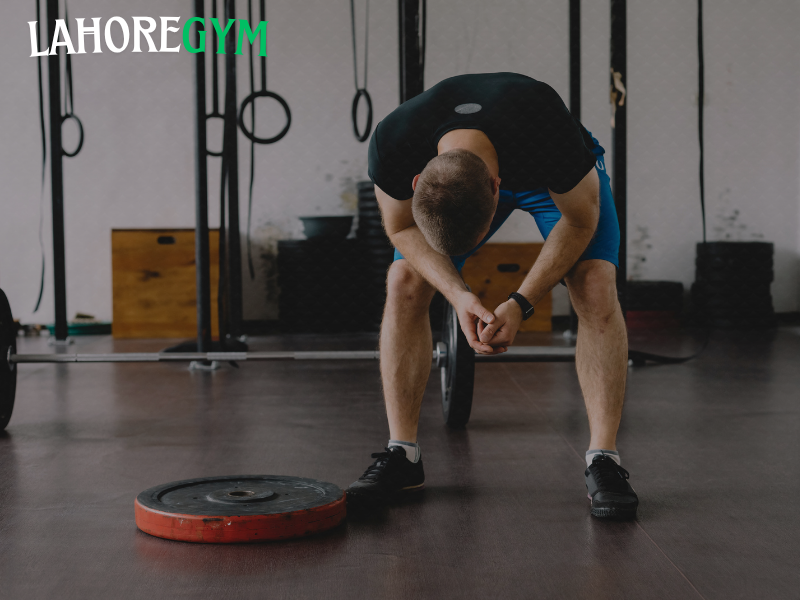 Exhausted athlete showing overtraining symptoms in the gym Tired male athlete sitting on gym floor after intense workout, showing signs of overtraining