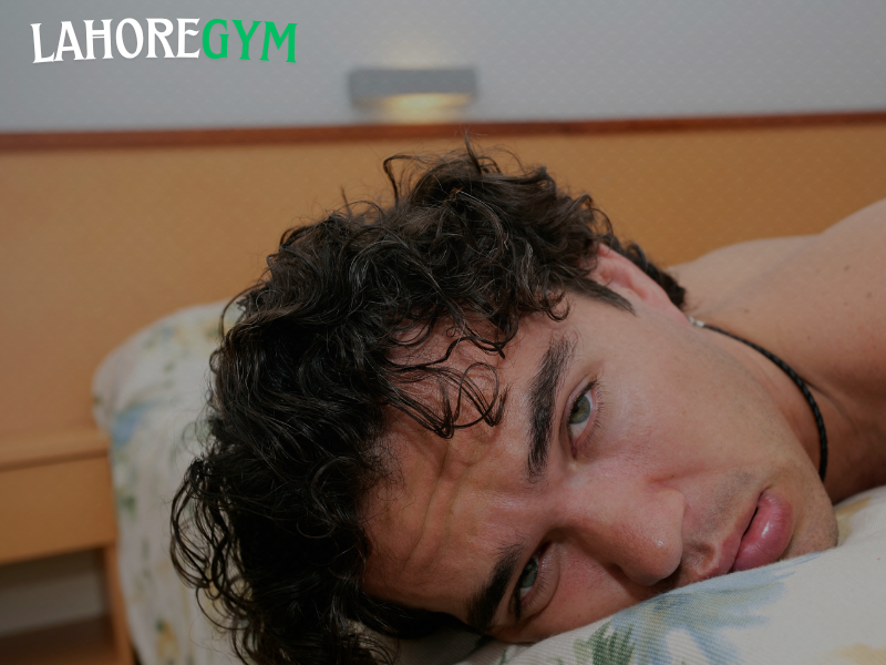 Poor Sleep Effects on Muscle Growth and Fat Loss A tired man sitting on a gym bench, looking exhausted after a workout, symbolizing how poor sleep affects muscle recovery and weight loss.