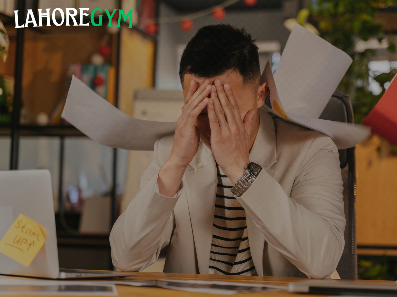 How Stress and Anxiety Affect Gym Progress A stressed-out man sitting in the gym with his head down, surrounded by weights